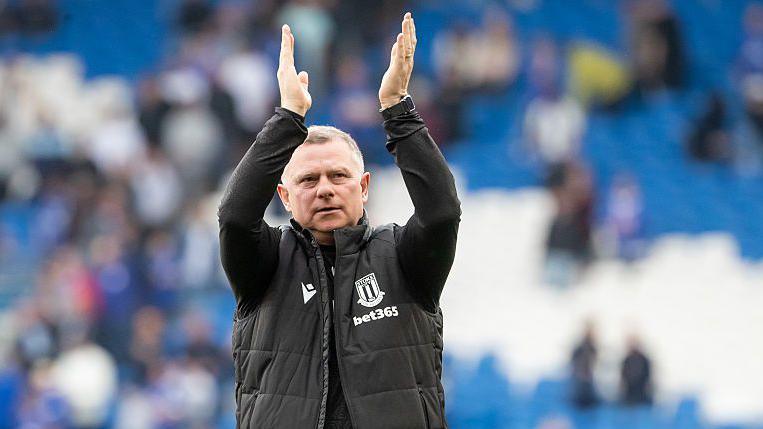 Stoke boss Mark Robins claps his hand above his head in appreciation to the club's fans after a game.
