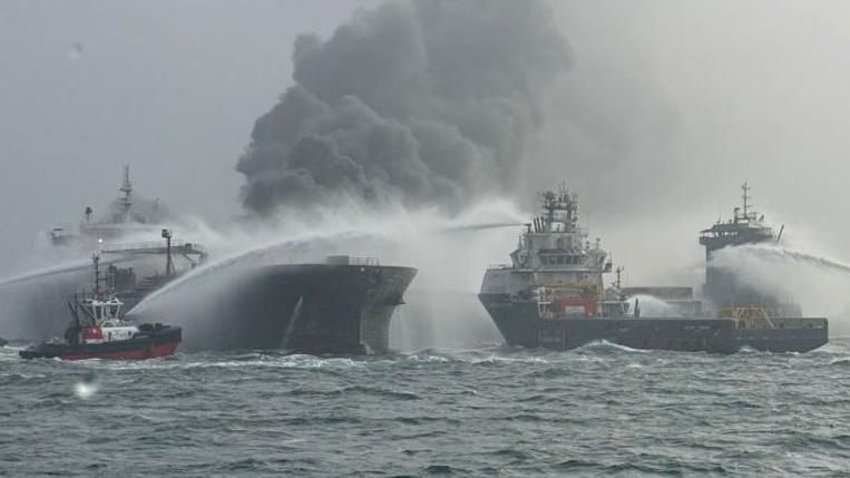 Tug boats shooting water at two burning ships in the North Sea