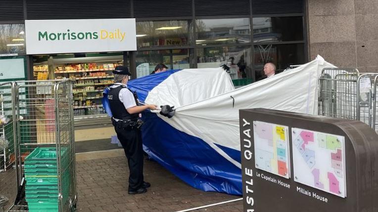 A police crime scene tent outside a supermarket