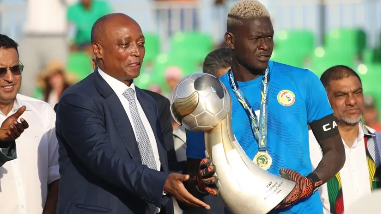 Patrice Motsepe in suit and tie hands the Caf Beach Soccer trophy to the winning captain, Senegal's goalkeeper, as other dignitaries stand and watch