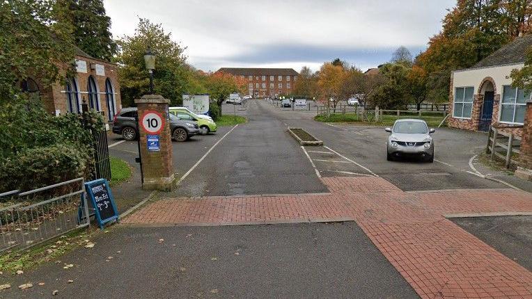 The entrance to Manby Park, with Bilney House in the background. There are gate posts and brick paving at the entrance.