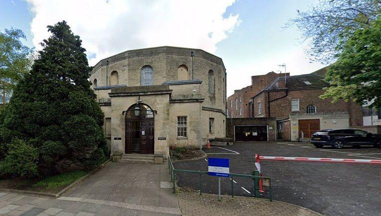 The exterior of Gloucester Crown Court on a clear day with cars parked in the car park and trees on the edge of the image