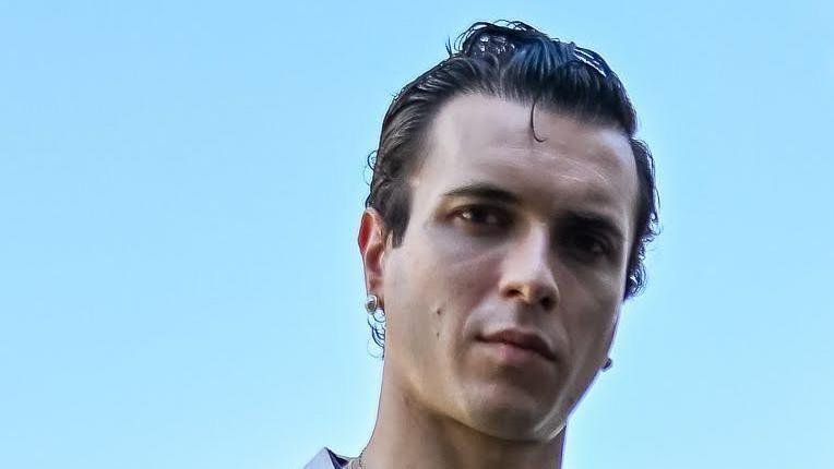 A close-up image of Ollie Trevers. He has dark hair that has been slicked back with Jel. He wears a silver earring in one ear.