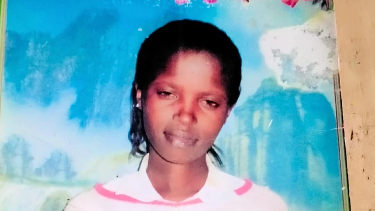 A young woman with dark skin smiling softly in a photo. Behind her is a large blue piece of wall