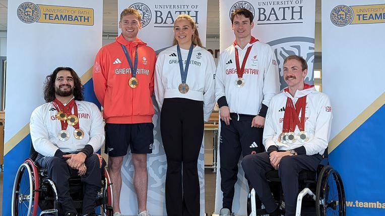 Left to right - Dimitri Coutya, Kieran Bird, Becky Wilde, Dan Bethell and Piers Gilliver. They are wearing their Olympic and Paralympic medals as well as Great Britain tops. They are in front of banners that read University of Bath and Team Bath.