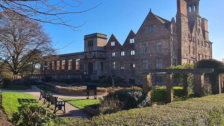 A publicity shot of Rufford Abbey, a historic building made of pinkish stone, with  the nearest part still roofed but most of the rest ruined