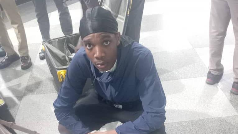 Tihaise Darlin Elisha, 19, crouched on the floor in the Robert Gabriel Mugabe International Airport. He is posing next to a large white suitcase that's filled with packets that contained the cannabis.