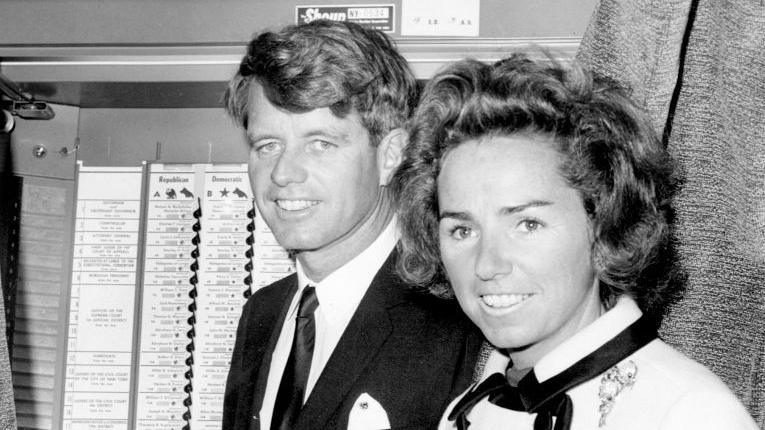 Senator Robert Kennedy enters a voting booth as his wife, Ethel, stands by