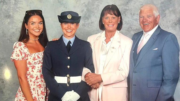 From left, a young woman wearing a white floral dress smiles at the camera while placing her hand on the shoulder of another young woman in an RAF graduation uniform smiles at the camera, linking arms with her mother next to her and Mr Ashcroft