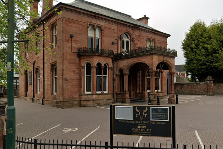 A redbrick building with a car park. A large sign sits at the entrance, with the name Cut visible.
