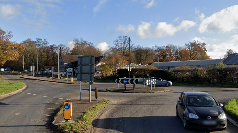 A roundabout road junction with a number of signs and cars.