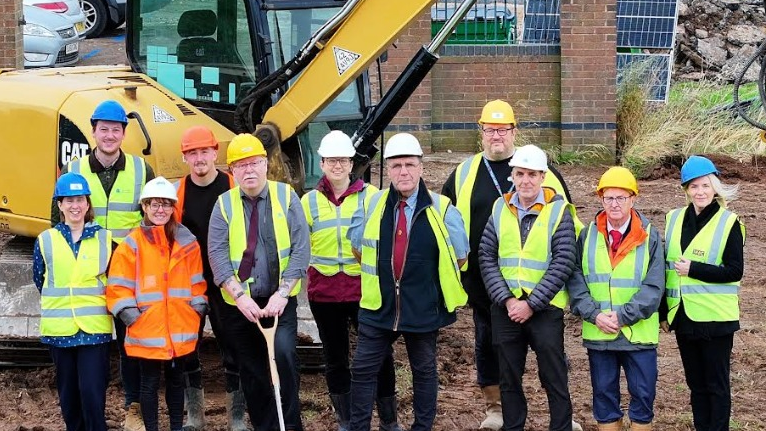 Several people in hard hats and high vis standing on a construction site infront of a yellow tractor