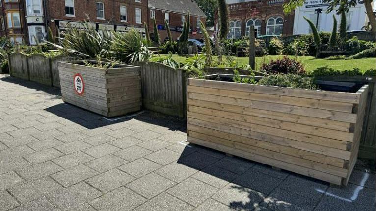 Two wooden flower planters on a pavement