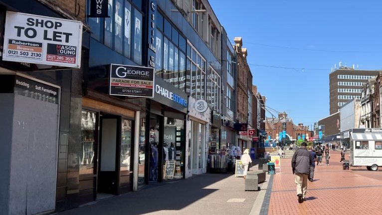 A high street with empty shops and people walking down the road