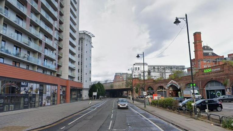 A car drives along the road, with high rise buildings at either side.