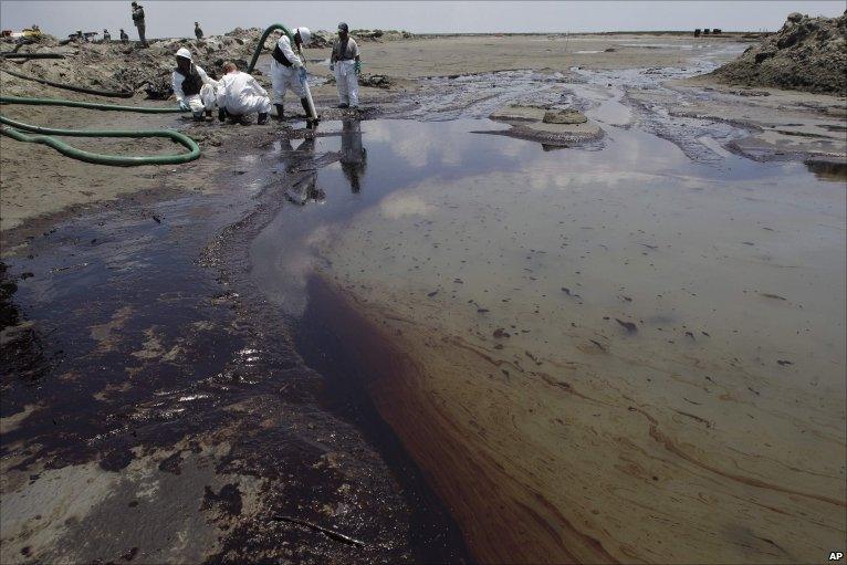 Workers use a suction hose to remove oil washed ashore from the Deepwater Horizon spill