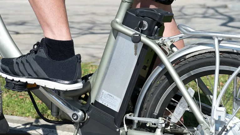 A close-up of a foot in a trainer, on the pedals of a silver e-bike