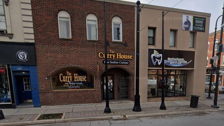 The exterior of a restaurant called the Curry House, a brick building set between two shops.