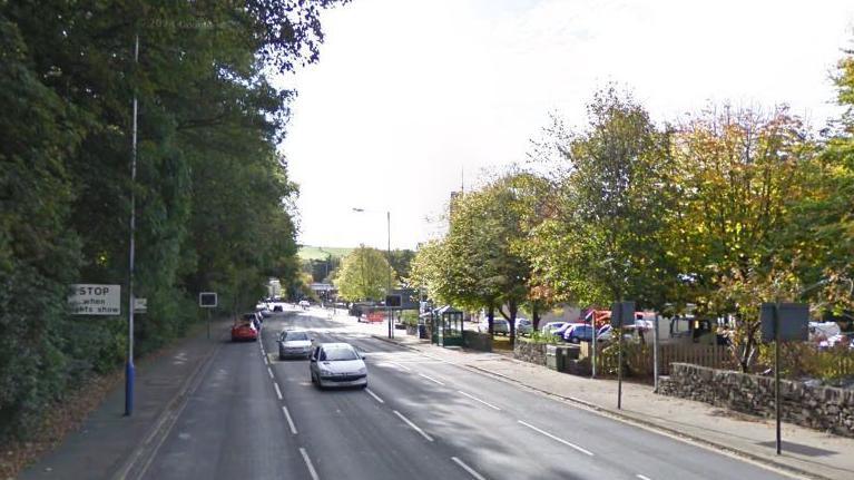 Peel Road is lined with trees as a few cars drive along it.