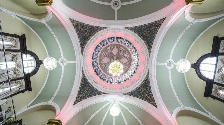 The view of the ceiling, looking up. It is circular with pink, blue green and dark green colours and different patterns. 