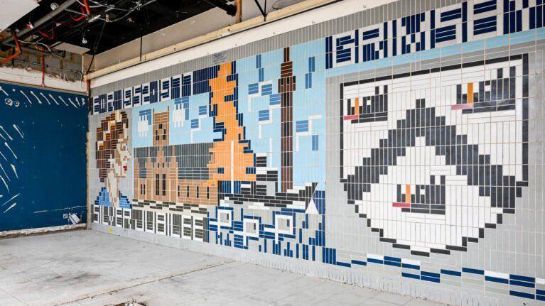 The tiles are thin and rectangular and are laid vertically. There is an image within the tiles design of the Queen, a church, a map of Great Britain and a coat of arms. Writing in the tiles says ER 1952.1977, Grimsby, Silver Jubilee.
