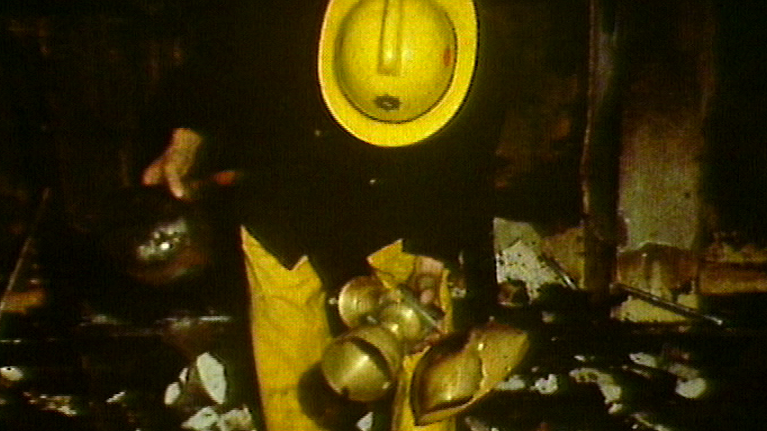 A firefighter wearing a yellow fireman's hat and fireman's uniform picking up damaged trophies.