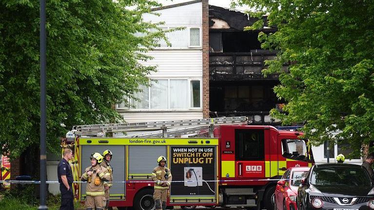 A fire engine and firefighters outside a burned-out residential building