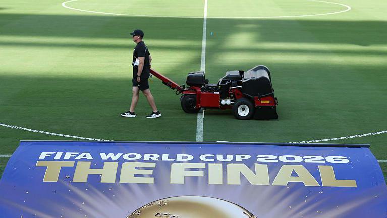 Staff attending to the field at the New York New Jersey Stadium with a sign for the 2026 World Cup final in the foreground