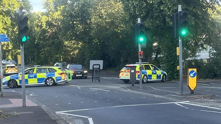 A police cordon in Hucknall Road near Nottingham City Hospital. Two police cars are blocking both sides of the road near a pedestrian crossing.