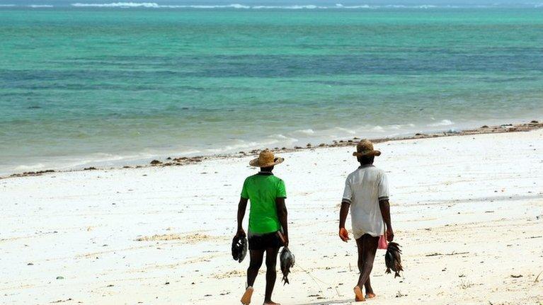 People walk along a beach in Zanzibar carrying fish