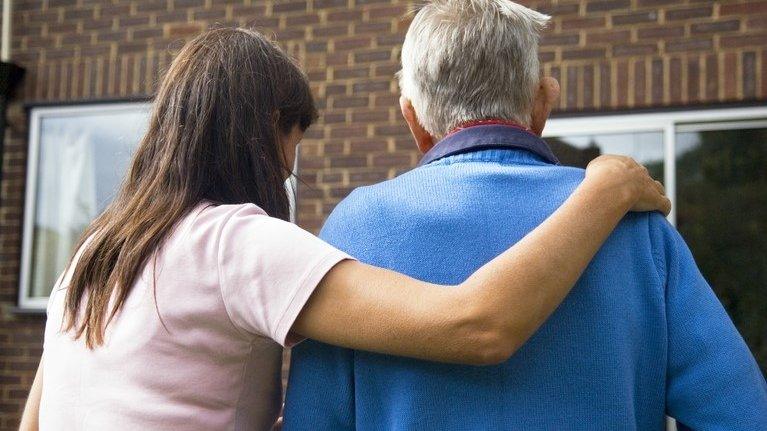 A young woman with her hand on an older man's shoulder, supporting him