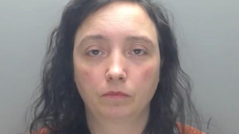 Mugshot of Paula Roberts. She has long black curly hair and her face is showing no emotion 