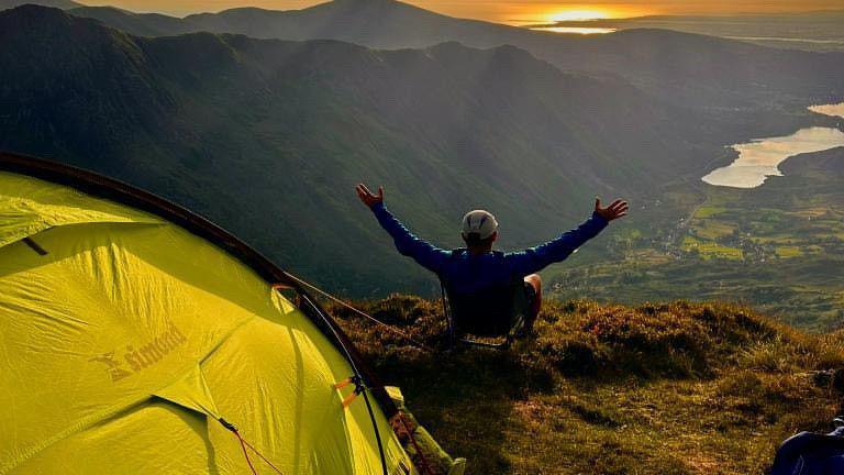 Tent pitched on clifftop with camper looking out over panoramic views