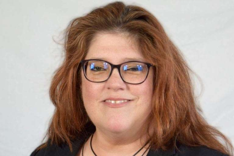 Sandra Squire is looking at the camera and smiling. She's wearing glasses and a black top and has long reddish brown hair.