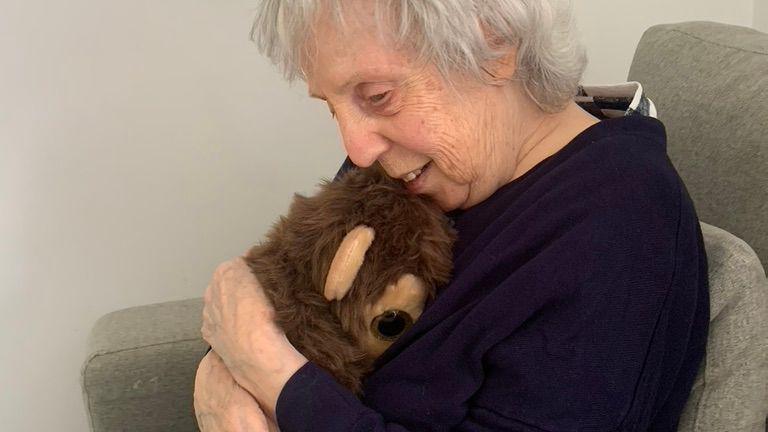 Vivian Harris sat up in a chair at the care home smiling as she cuddles a toy bear.