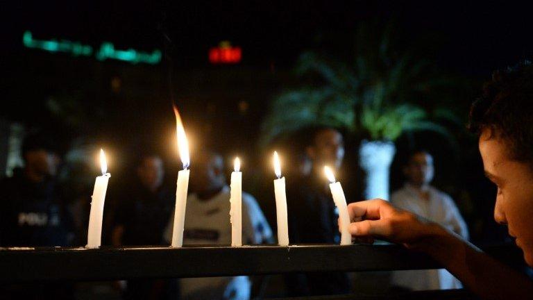 A boy arranges candle lights on a fence in front of the Hotel Imperial Marhaba in Sousse