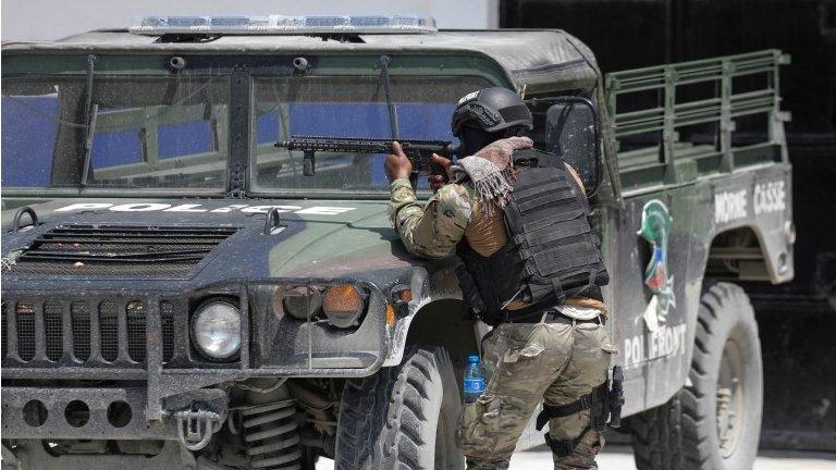 A member of the Haitian National Police takes cover behind a police vehicle while patrolling as ongoing gun battles between rival gangs have forced residents to flee their homes, in Port-Au-Prince, Haiti April 28, 2022