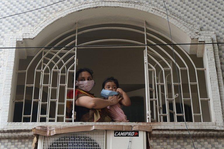 A resident along with her child wearing face mask stands in front of a window during a government-imposed nationwide lockdown in Chennai on June 29, 2020