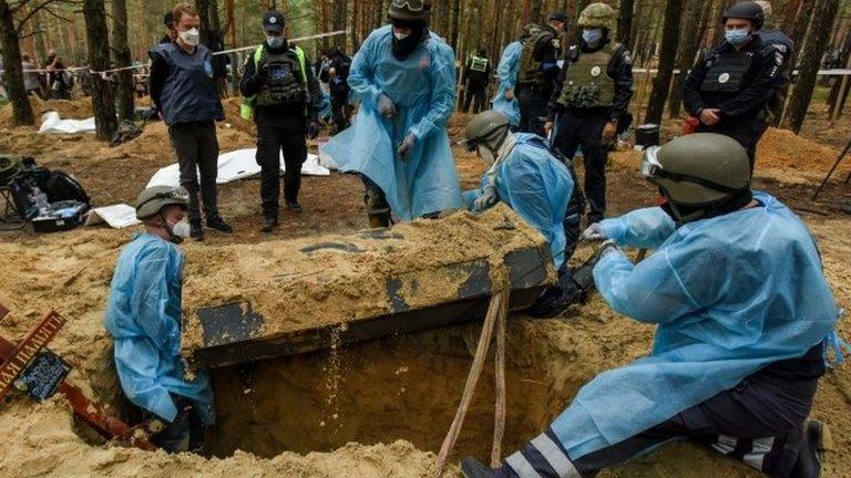 Emergency workers take a coffin out of a grave