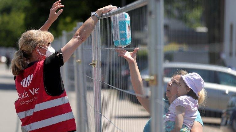 A volunteer hands nappies to a woman and her child over a fence in Guetersloh