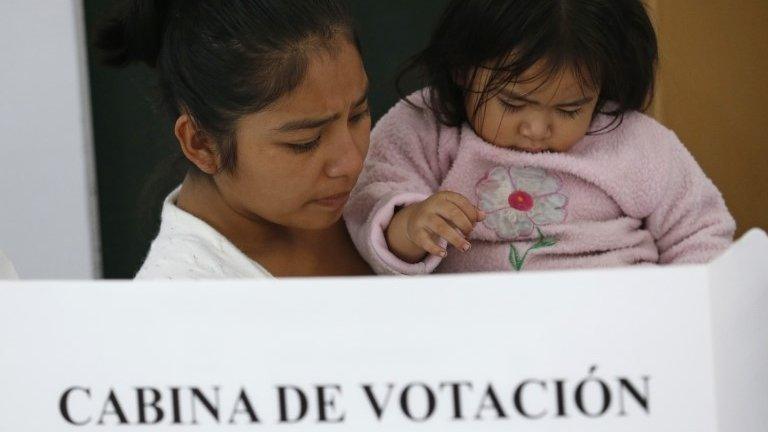 A woman carries a baby as she votes at a polling station during the presidential runoff election in Lima, Peru, Sunday, June 5, 2016.