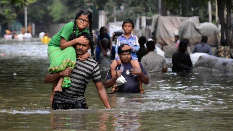 Indian residents carry children as they walk through floodwaters in Chennai on December 3, 2015