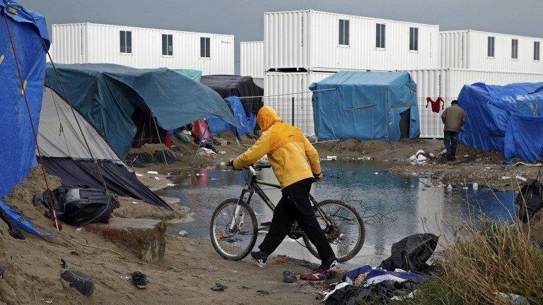 A migrant walks among tents in a makeshift camp as containers are put into place to house several hundred migrants living in what is known as the "Jungle"