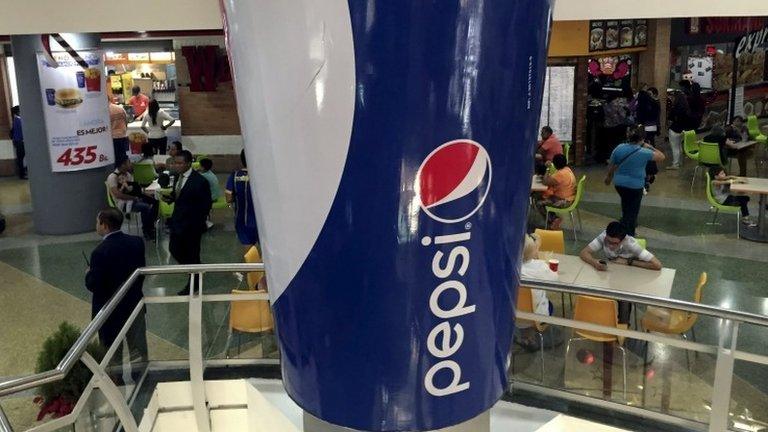 People walk past a mock giant cup of soda, part of a publicity campaign of Pepsi, at a shopping mall in Caracas on 20 December, 2015.