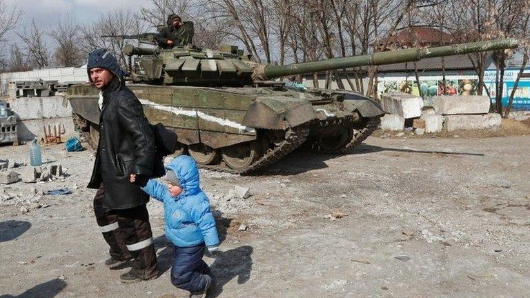 A local resident walks with a child past a tank of pro-Russian troops in the besieged city of Mariupol