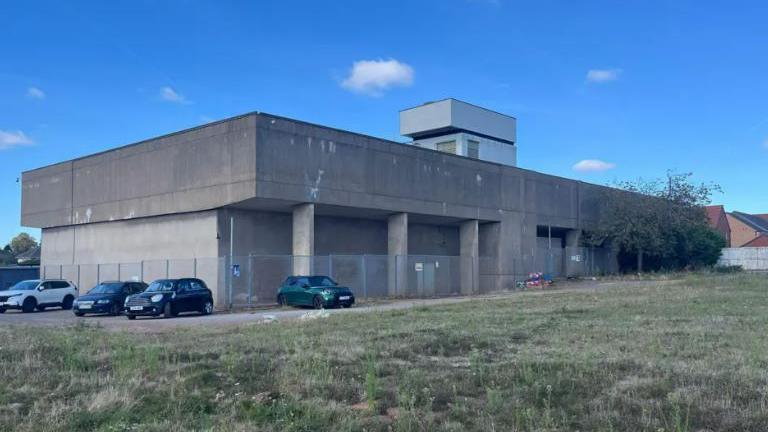 A concrete building with four cars parked outside. 