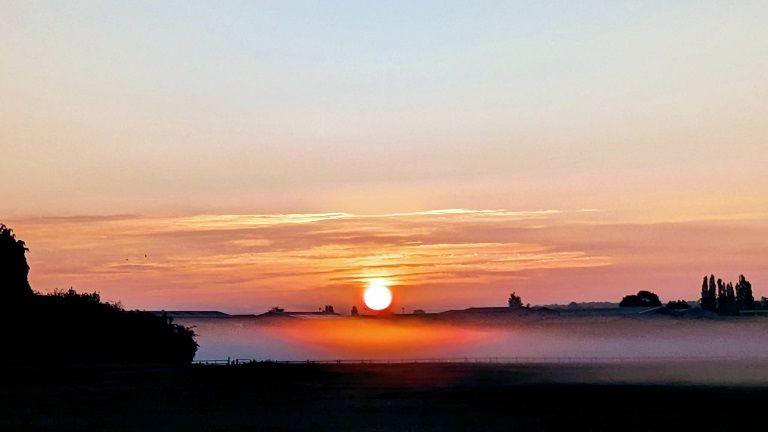 The sun sets in a sky with a white ball in the centre of a sky coloured red, yellow and orange.
