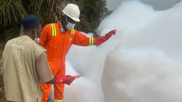 Two officials in Nigeria stand next a white foam substance on Abuja-Kaduna highway