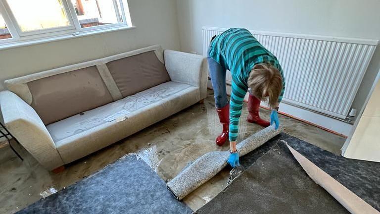 Woman in wellies rolls up wet carpet 