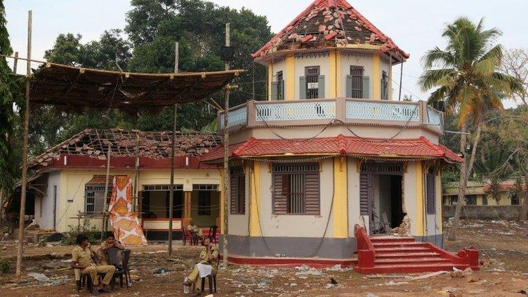 Indian policemen guard the damaged structures at the spot where a massive fire broke out during a fireworks display at the Puttingal temple complex in Paravoor village, Kollam district, southern Kerala state, India, Monday, April 11, 2016